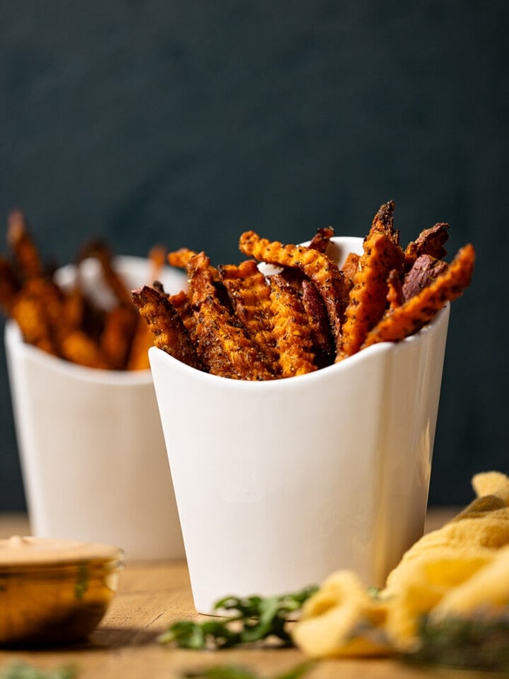 Sweet potato fries in fry holders on a wood table with green background.