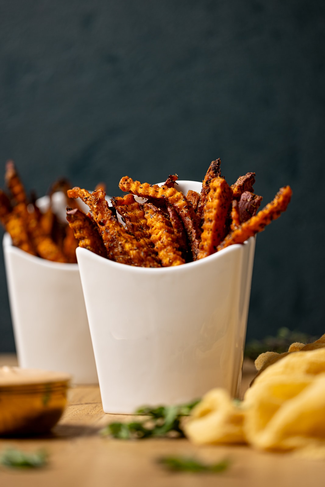 Fries in two white fry holders with herbs and a yellow napkin.