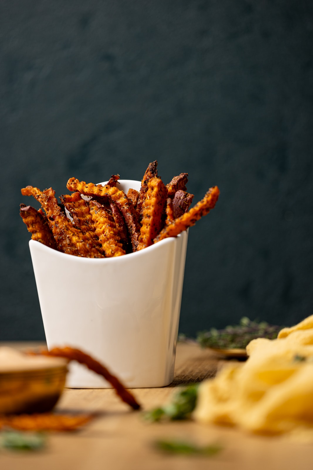 Fries in a fry holder with dipping sauce and a dark green background.