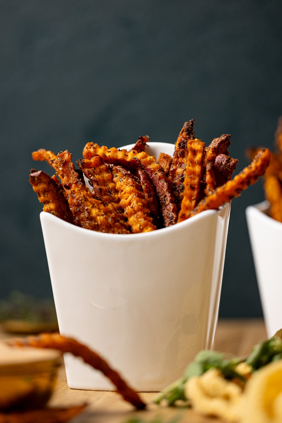 French fries in a white fry holder with sauce and a dark green background.