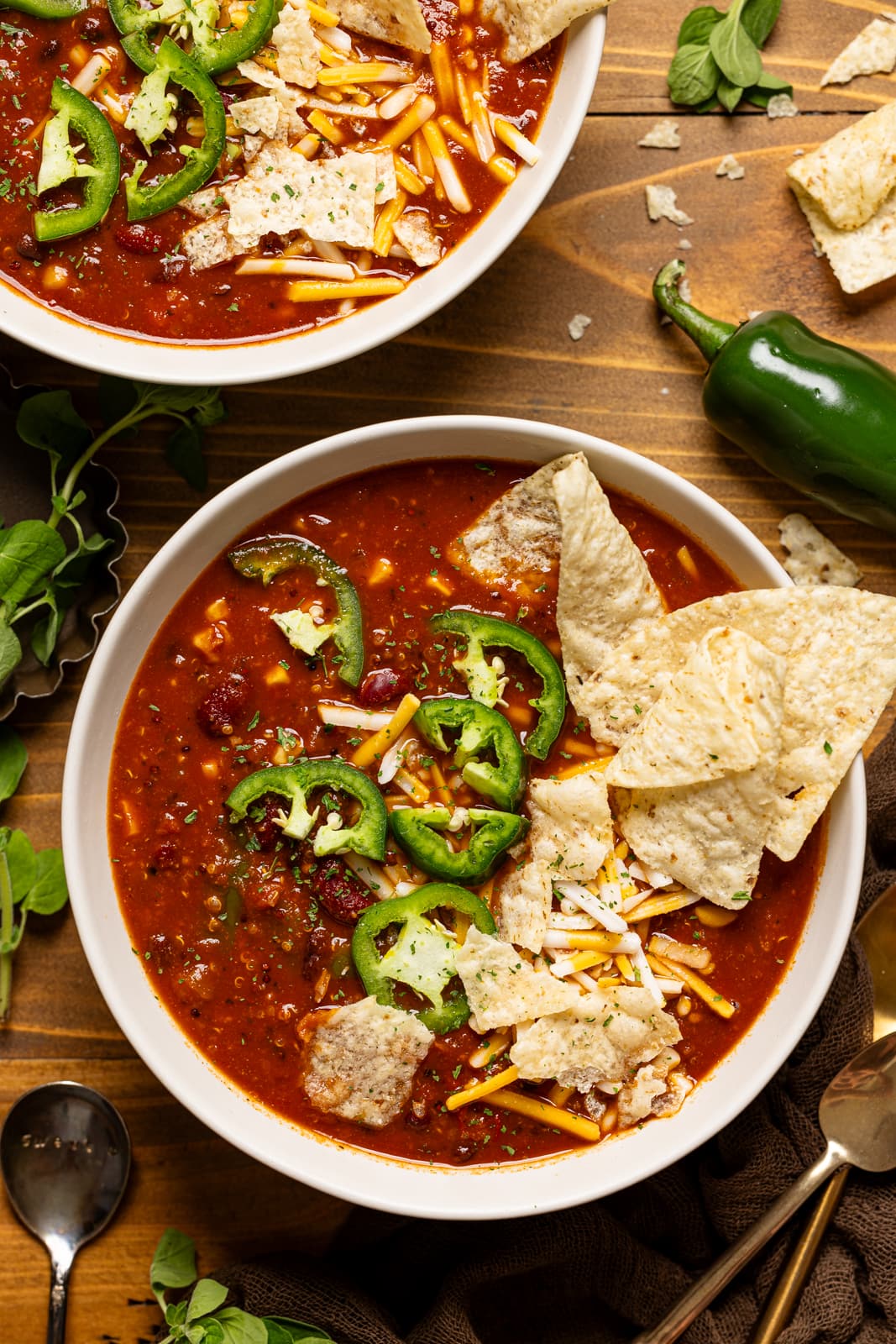 Two bowls of soup with tortilla chips, jalapeños, and spoons.