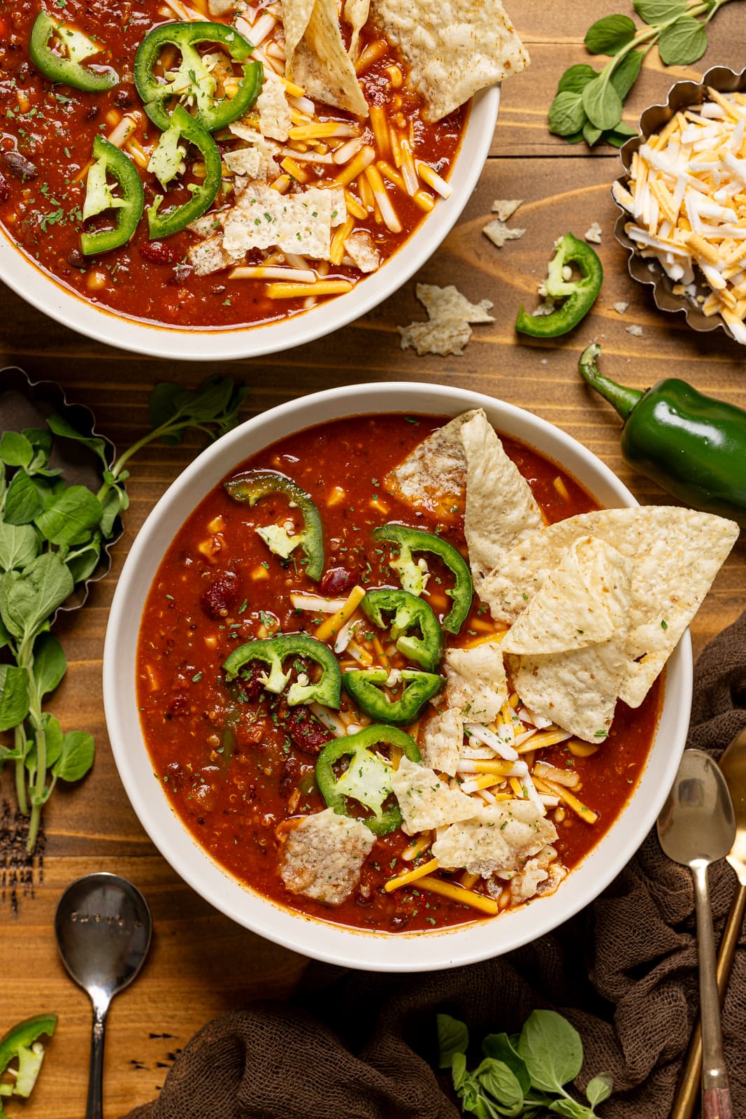 Two bowls of vegan taco soup with spoons and tortilla chips.