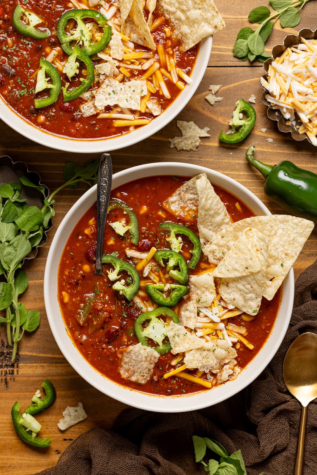 Bowls of vegan taco soup on a brown wood table with a spoon and cheese, jalapeños, and spoons.