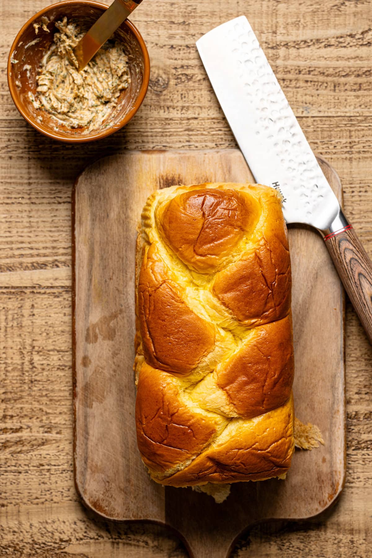 Loaf of brioche bread on a cutting board with a knife and herb butter.