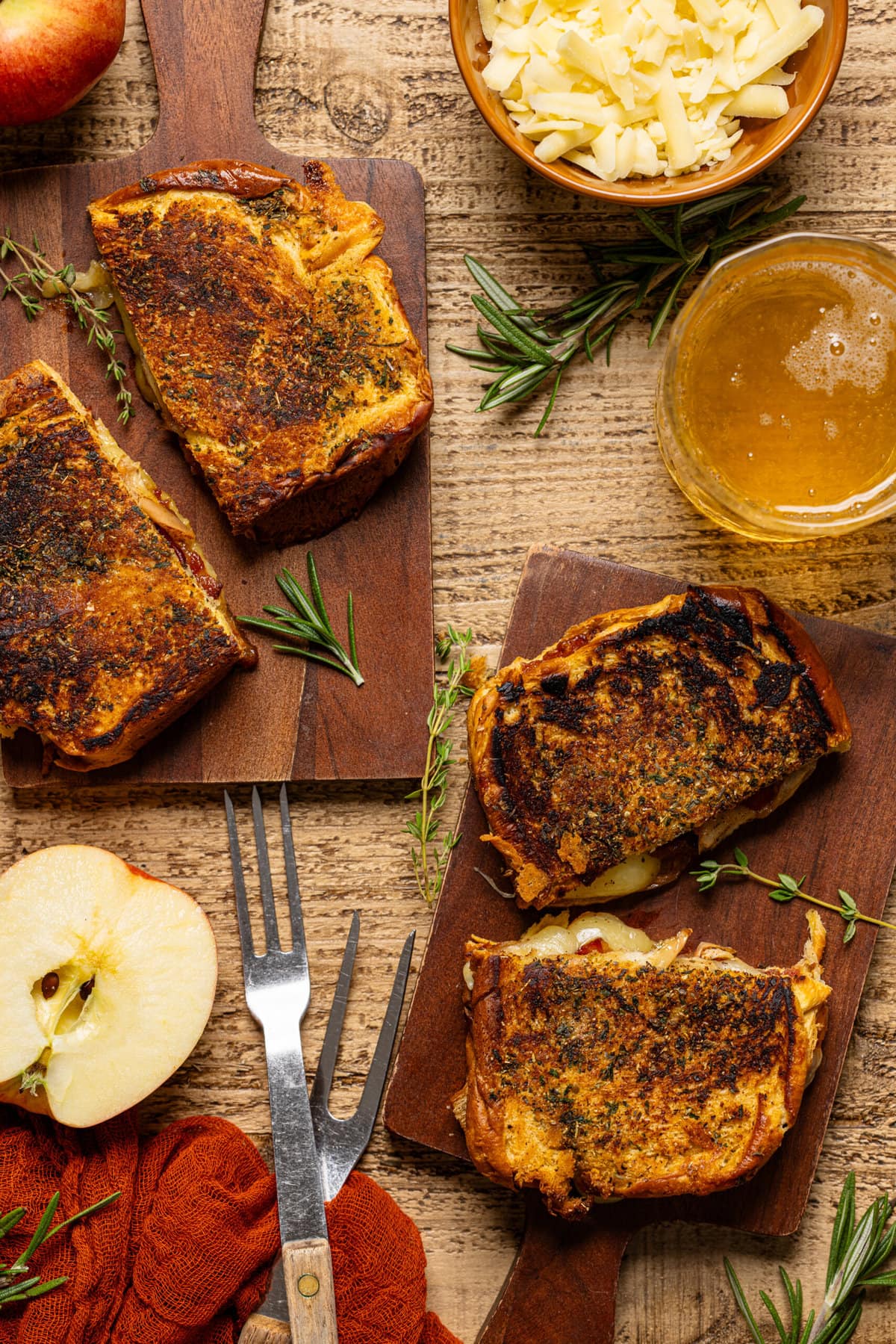 Grilled cheeses sliced on brown serving boards with a drink, two forks, and apples.