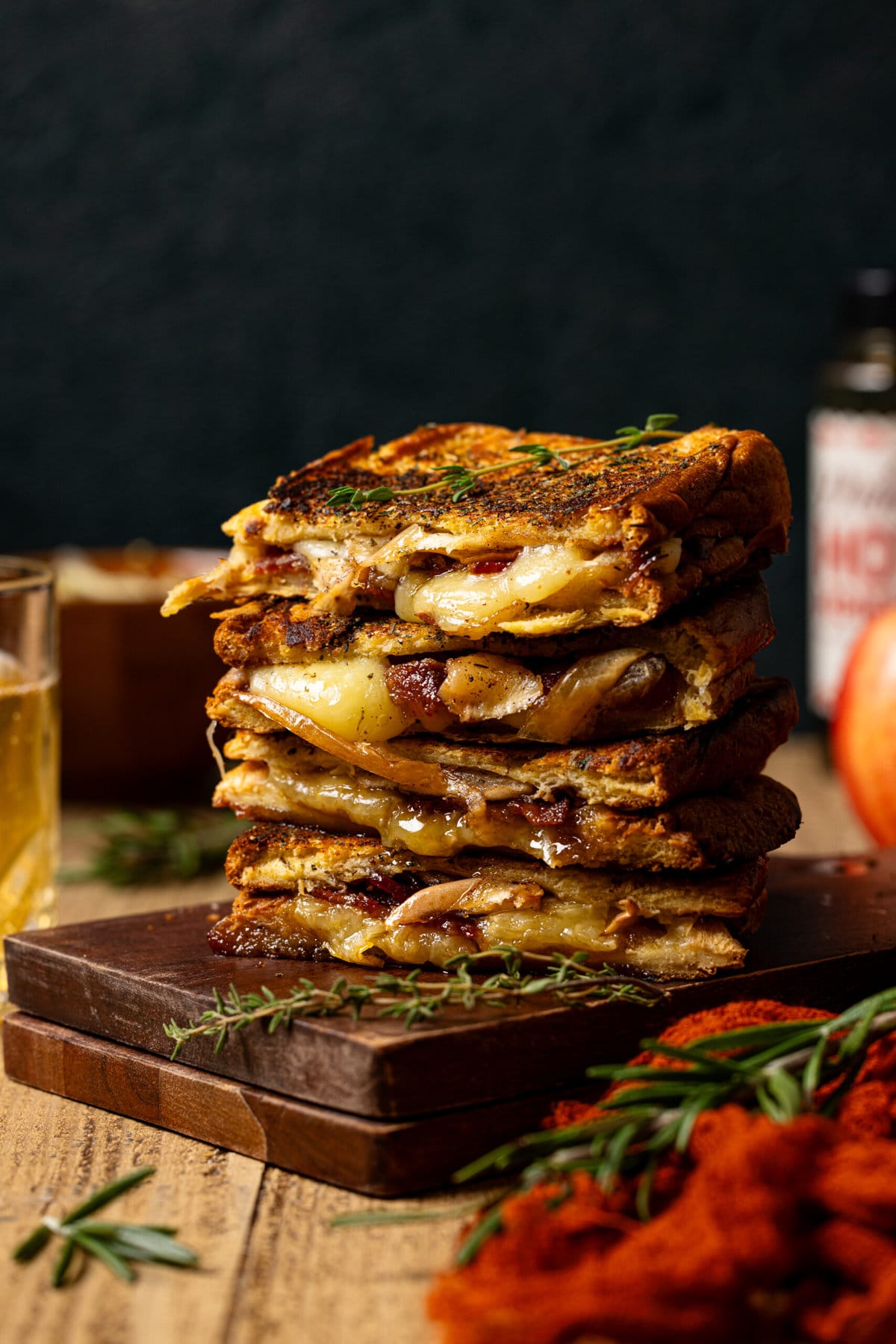 Stack of grilled cheese on a brown board with hot honey and apple in background. 
