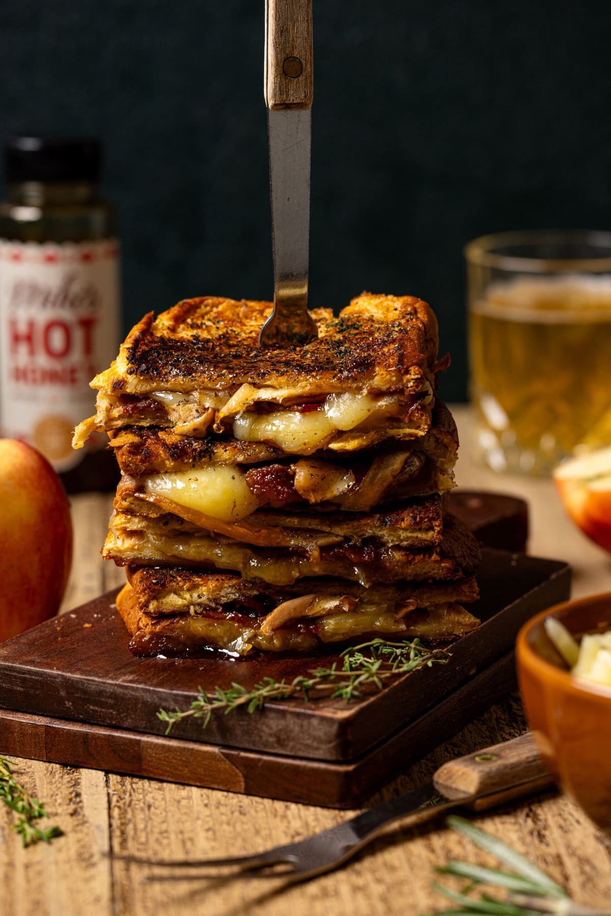Stack of grilled cheese with apple, hot honey, drink, and bowl of cheese.