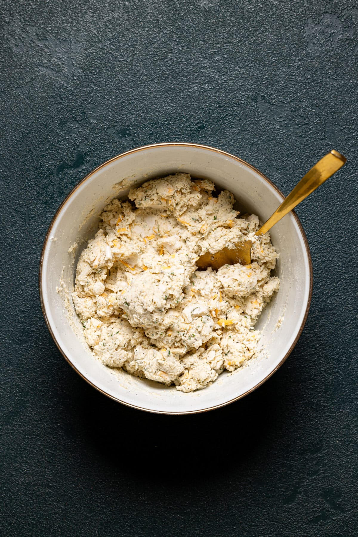 Biscuit dough in a white bowl with gold spoon.