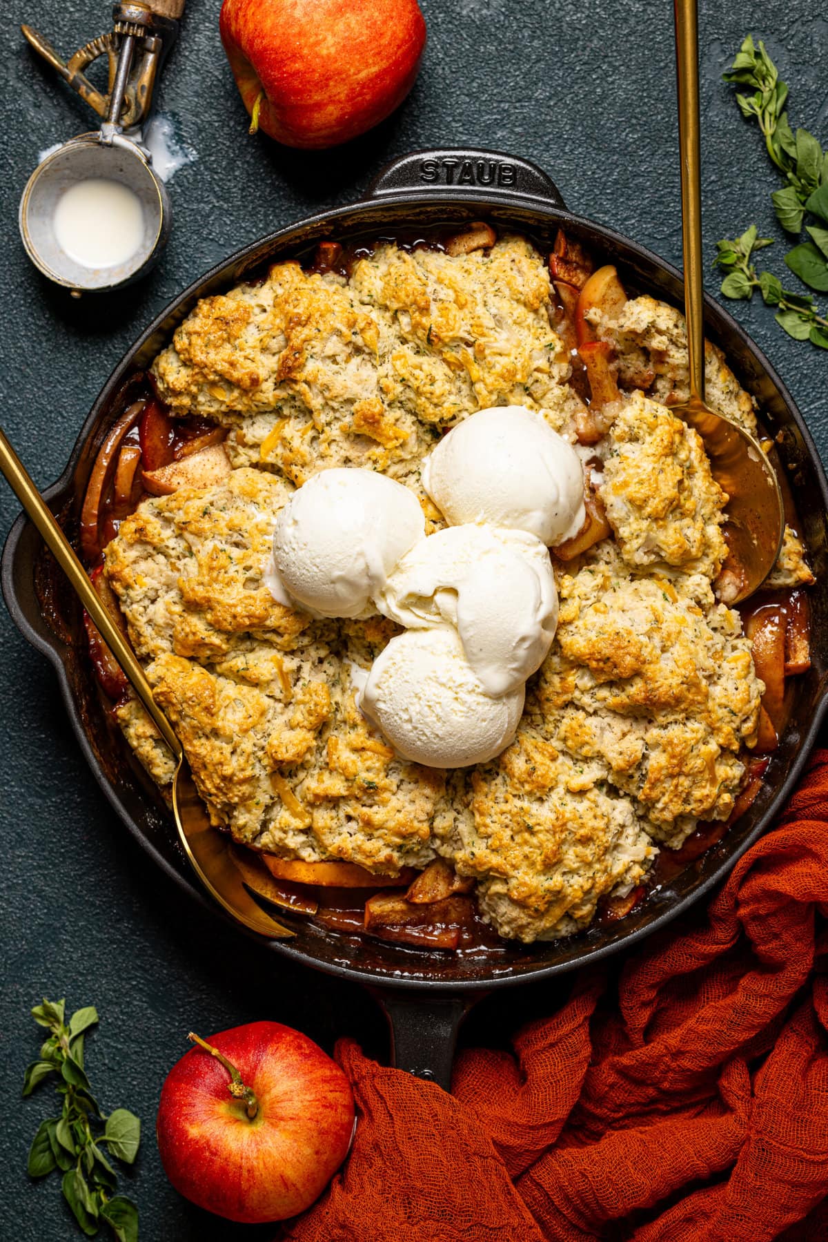 Baked cobbler in a skillet with two serving spoons and scoops of ice cream.