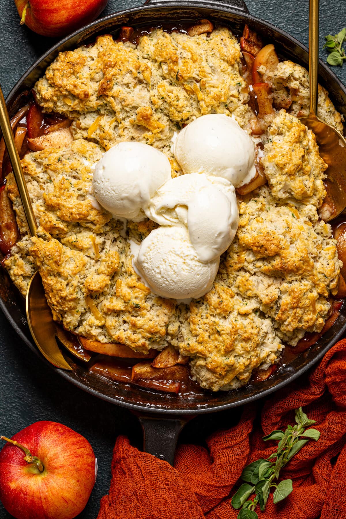 Up close shot of baked cobbler with scoops of ice cream and serving spoons.
