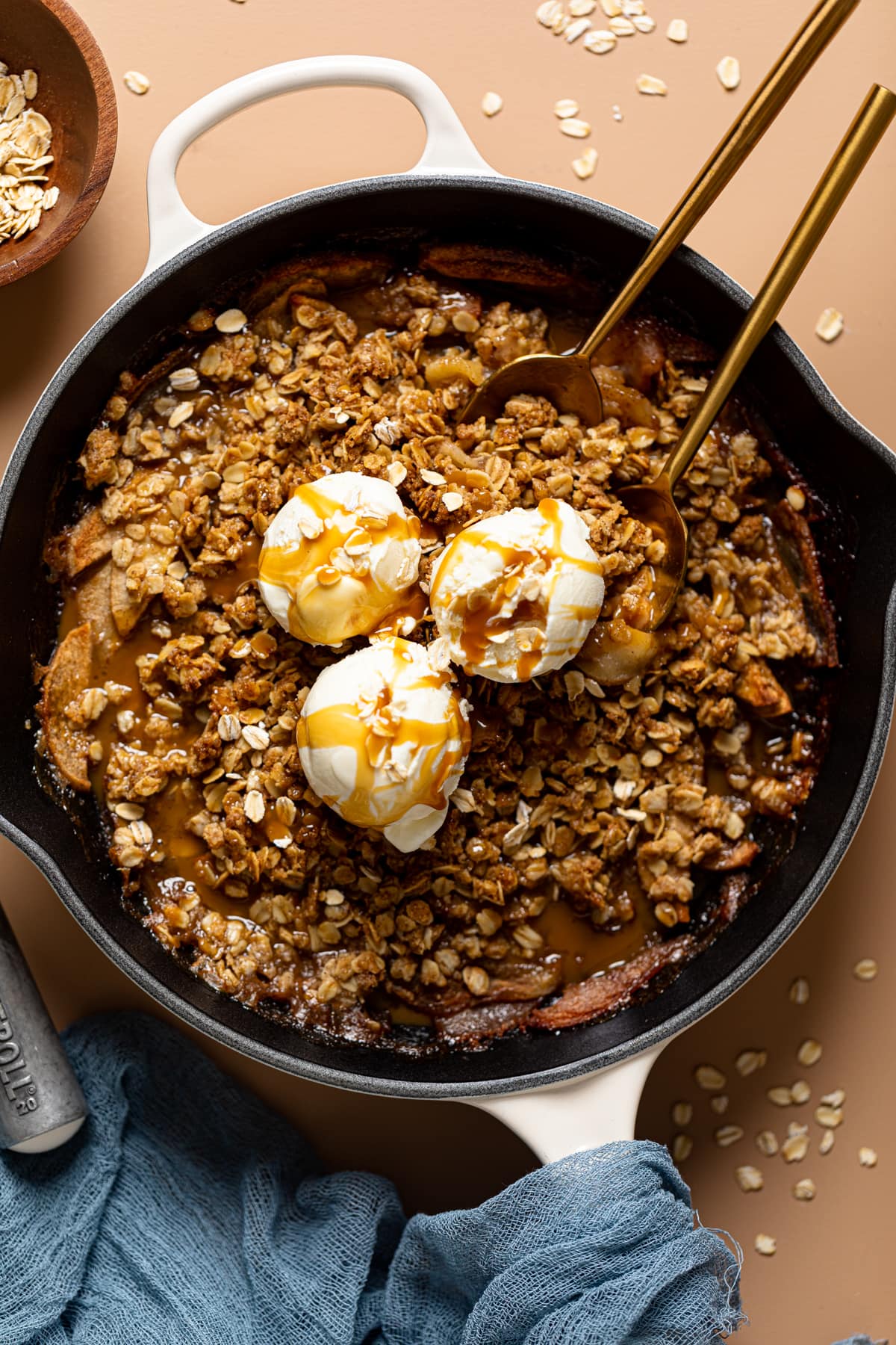 Homemade apple crisp in a white skillet with two spoons and ice cream as topping.
