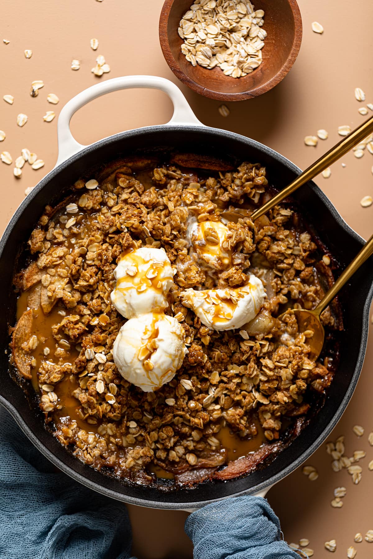 Homemade crisp with ice cream topping and two spoons with oats in a bowl.