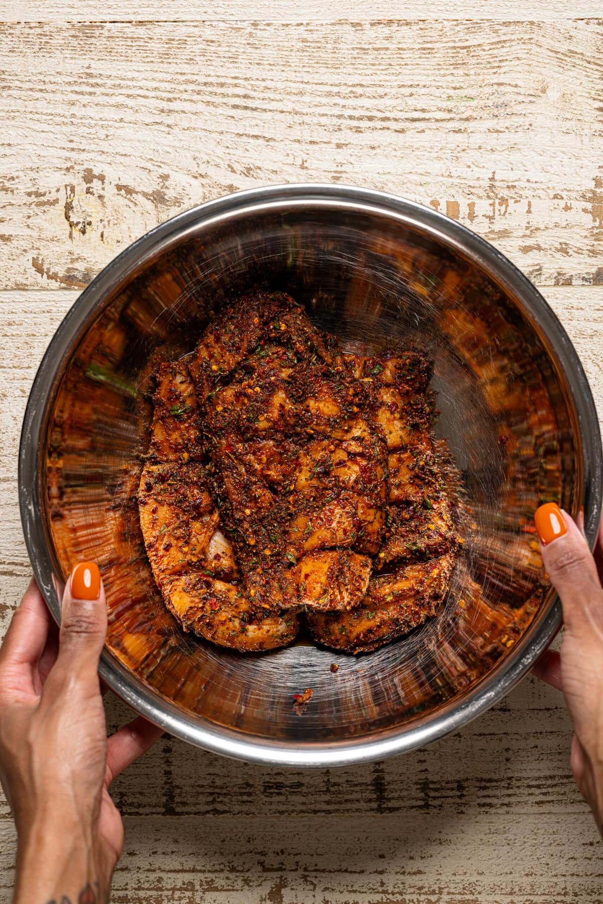 Marinated chicken in a silver bowl being held. 