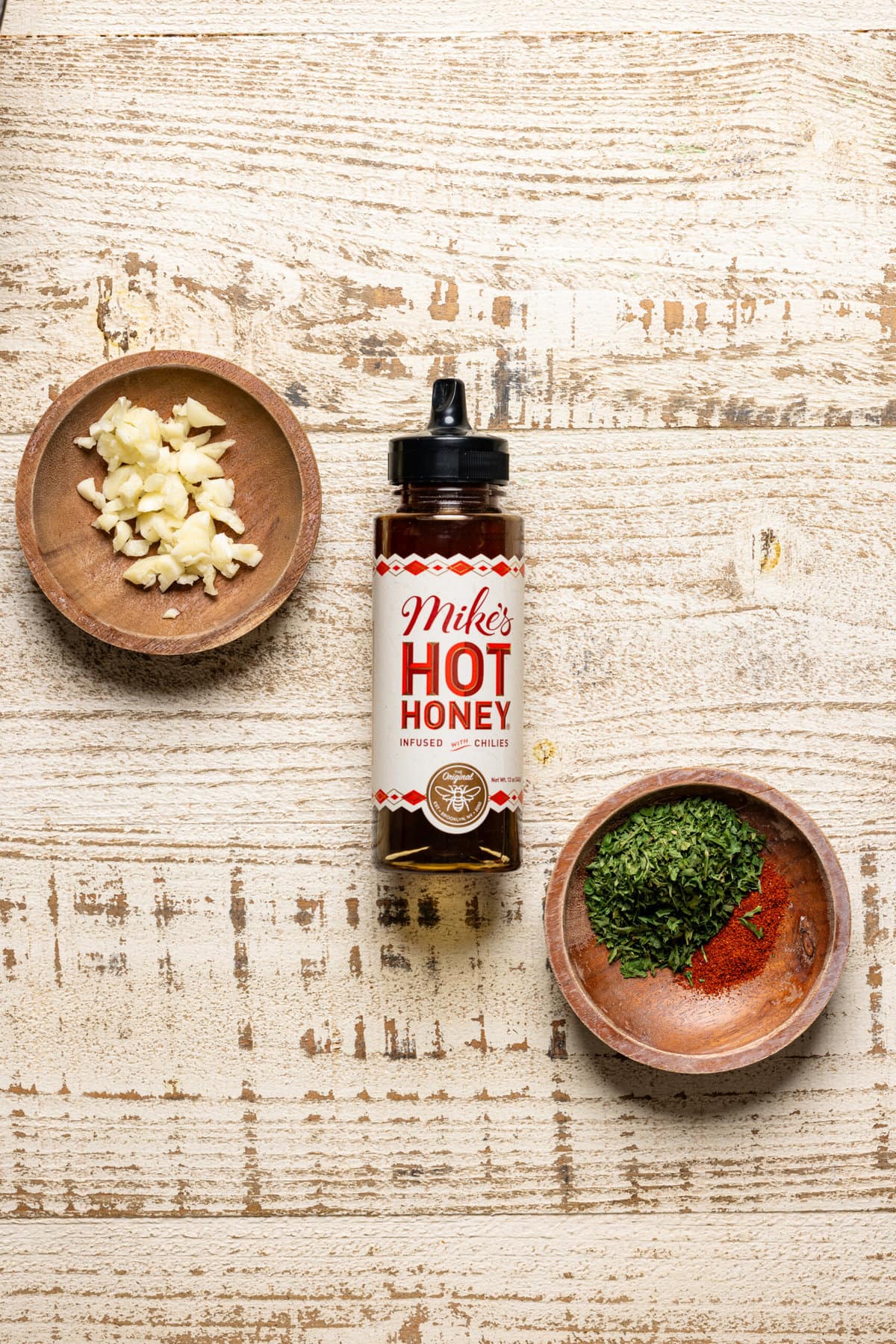 Hot honey sauce, garlic, and herbs + seasonings on a white wood table. 