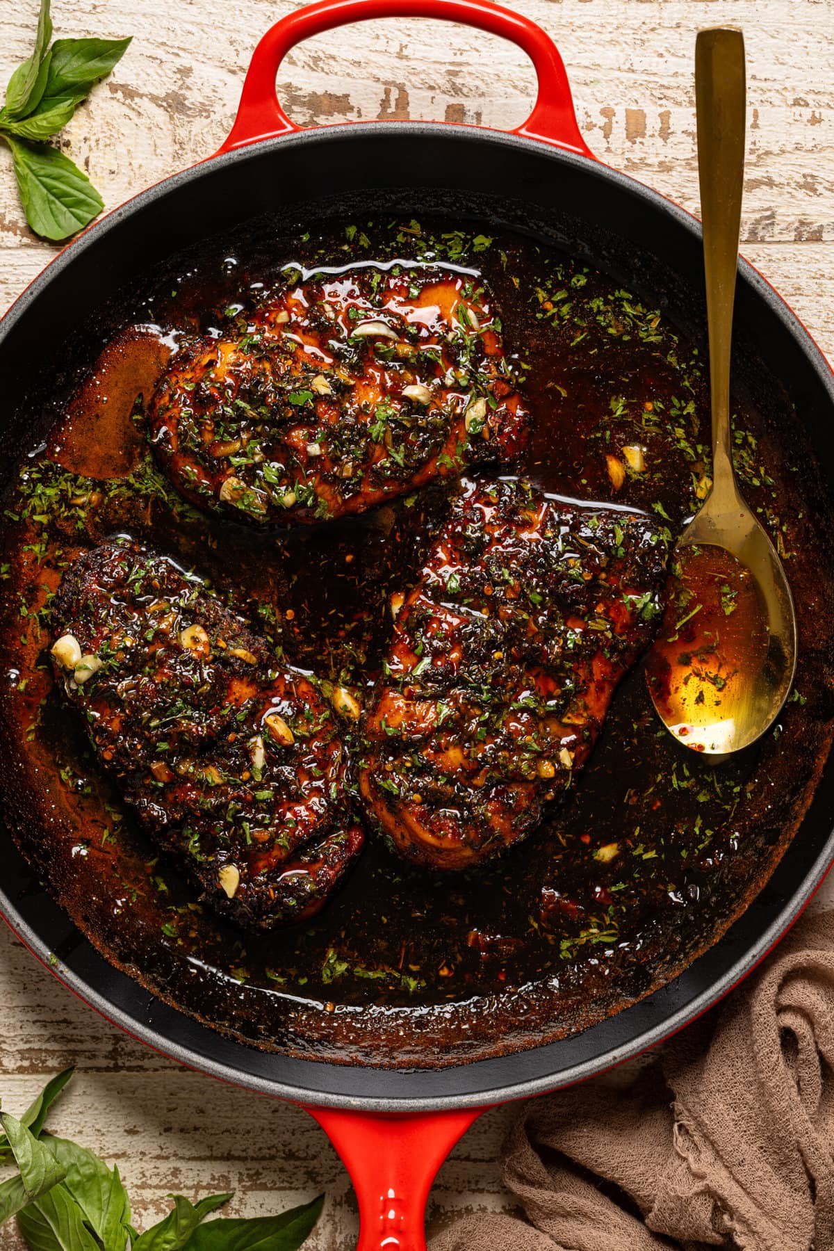Chicken breasts in a red skillet with gold spoon.