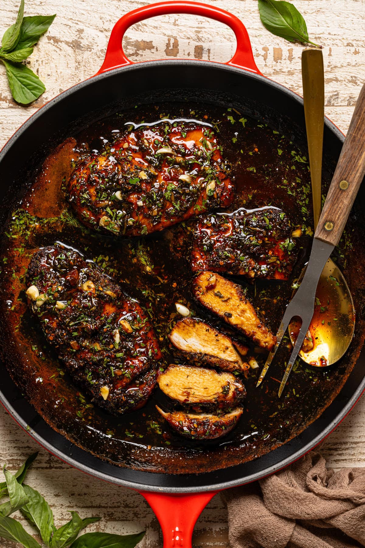 Chicken breasts in a red skillet with a spoon and fork.