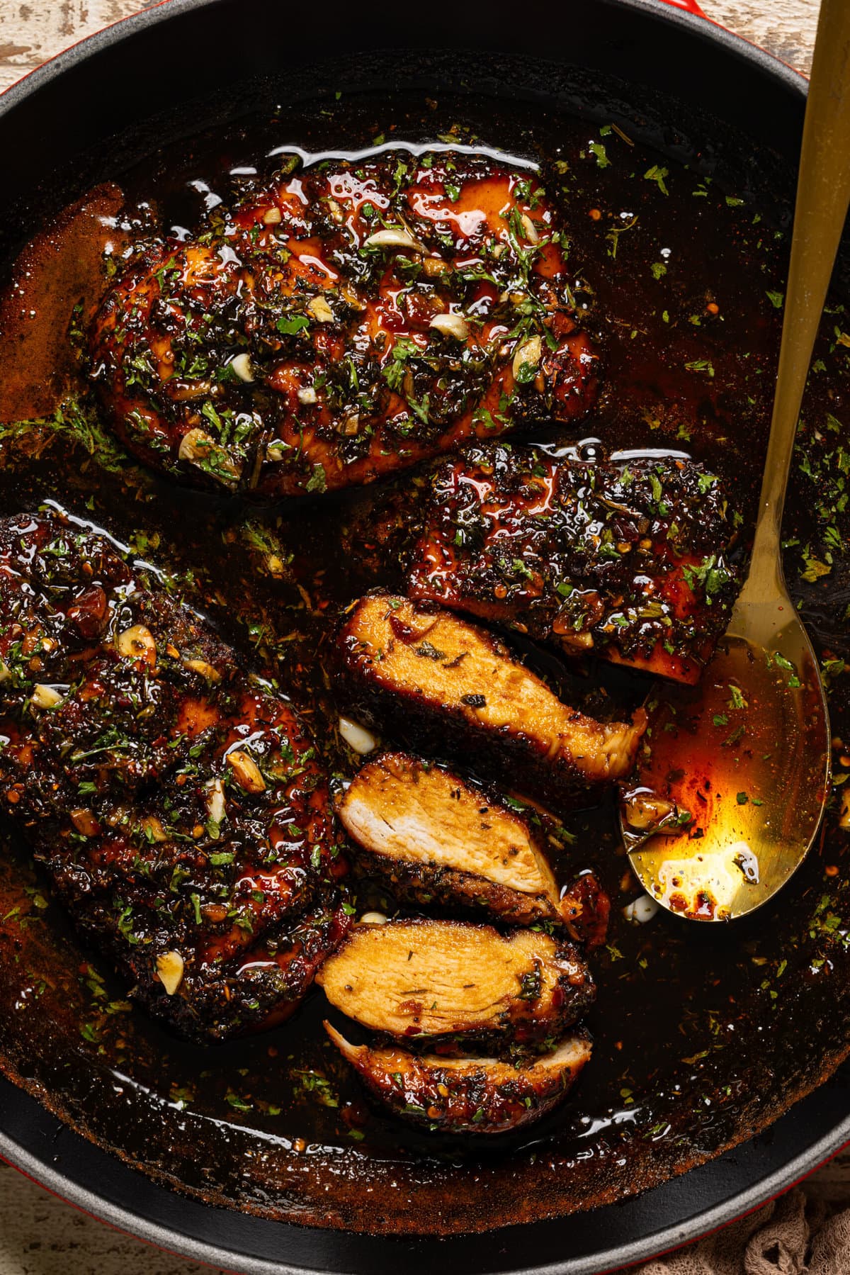 Chicken breasts in a skillet, half sliced with a gold spoon.