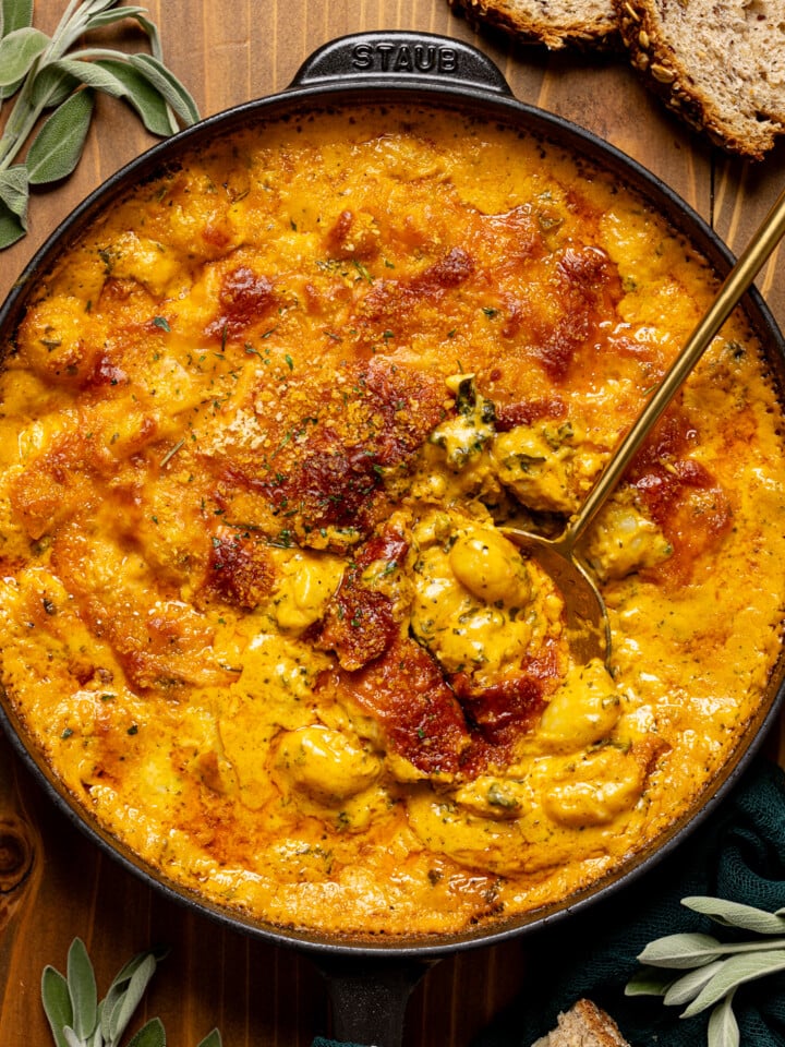 Baked gnocchi in a black skillet with a gold spoon, herbs, and pieces of bread.