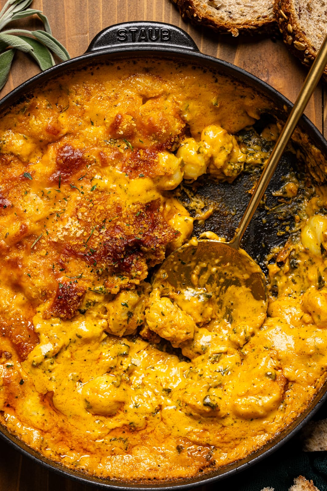 Baked pumpkin gnocchi in a black skillet scooped with a golden spoon.