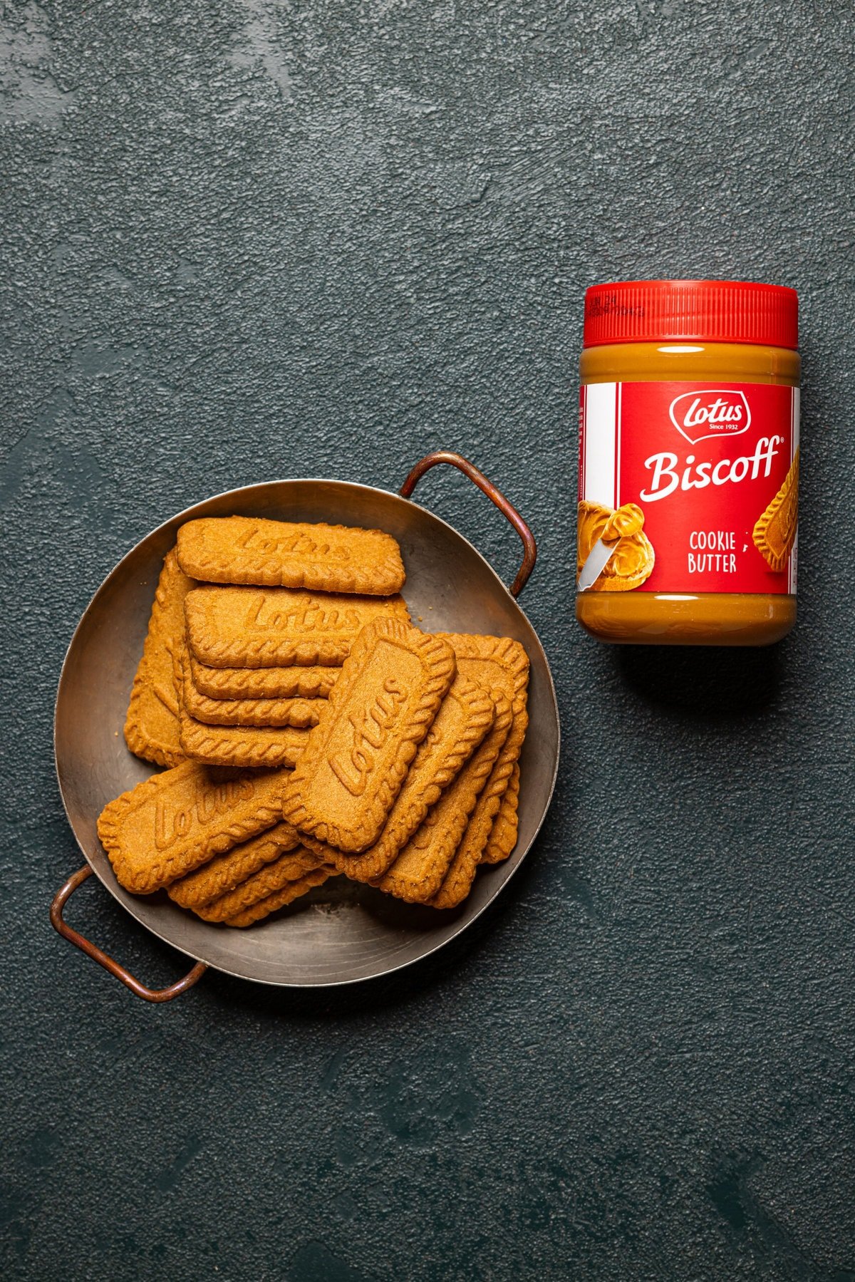 Biscoff cookies and cookie butter on a dark green table.