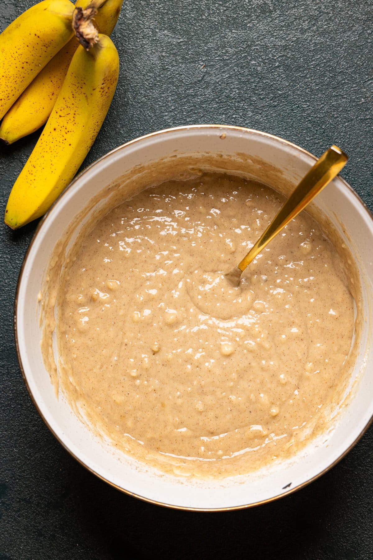 Bowl of batter with a spoon and bananas.