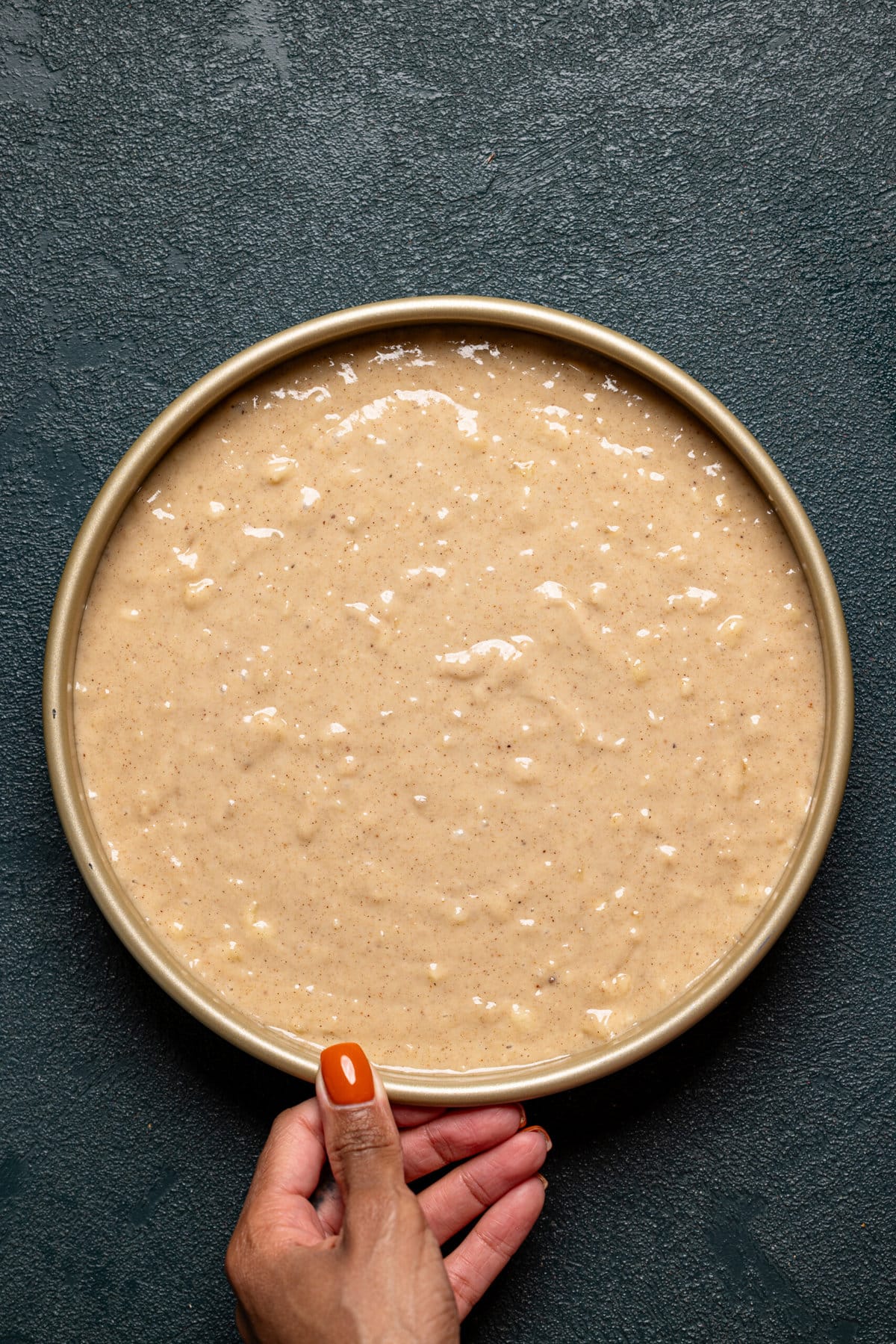 Cake batter recipe in a round cake pan being held.