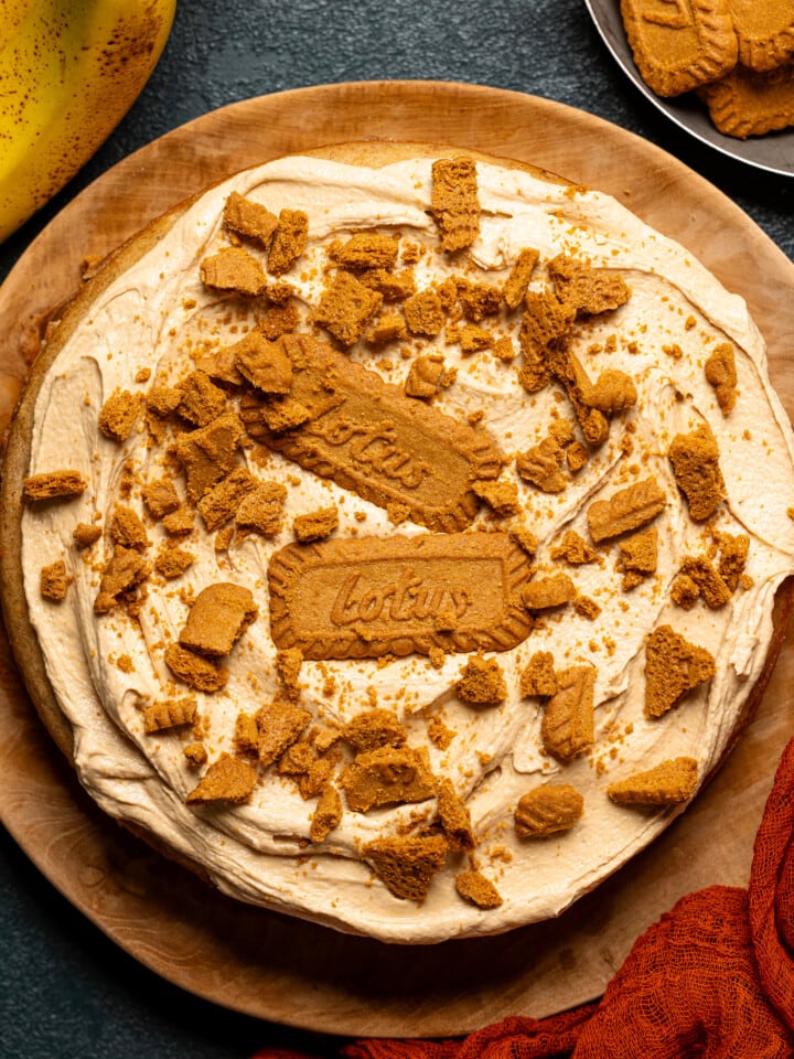 Cake on a wooden serving plate with toppings of biscoff cookies.