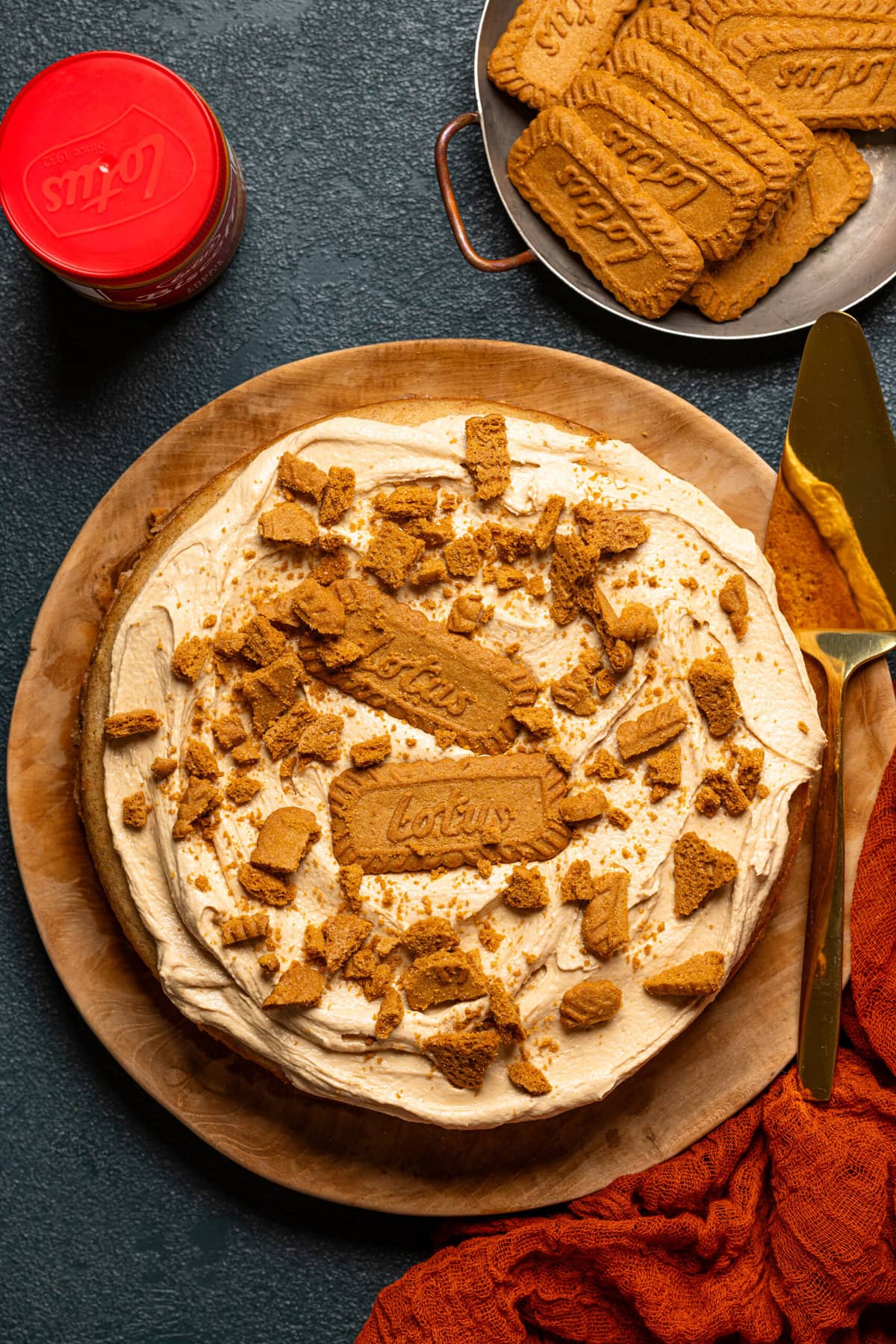 Biscoff cake on a wooden serving table with a serving spatula, cookies, and jar of biscoff cookie butter.