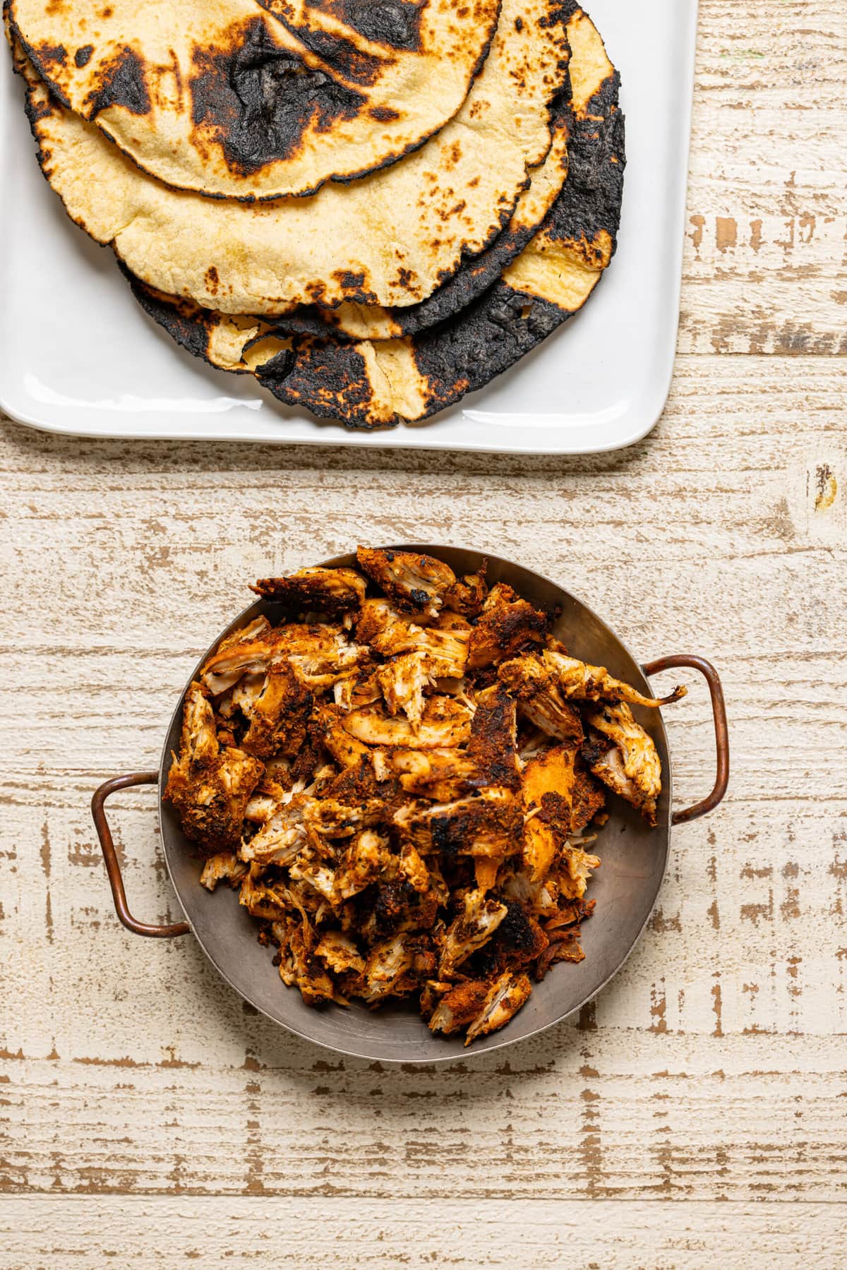 Shredded blackened chicken in a bowl and charred tortillas.