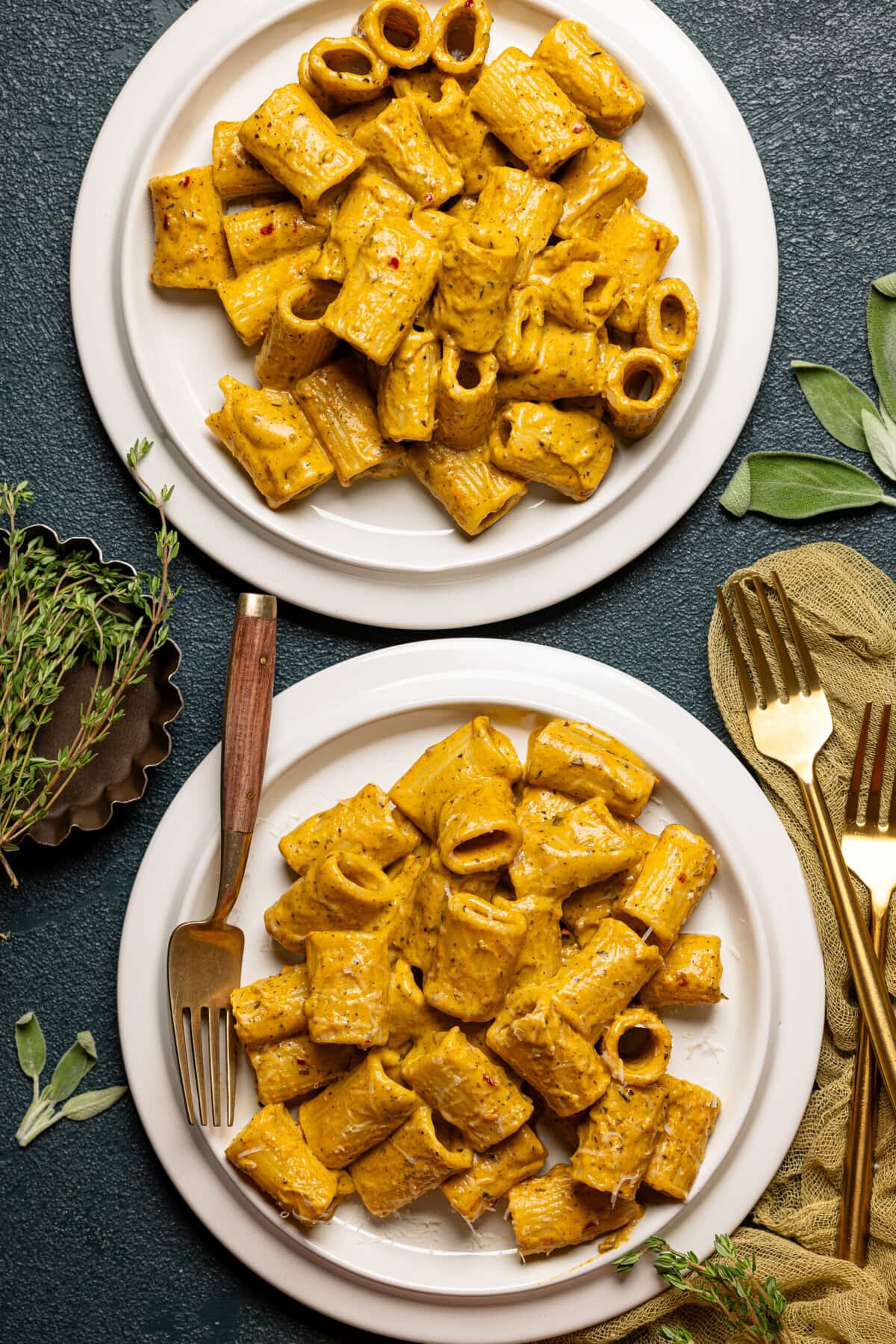 Two plates of butternut squash pasta with a fork and a side of two forks.