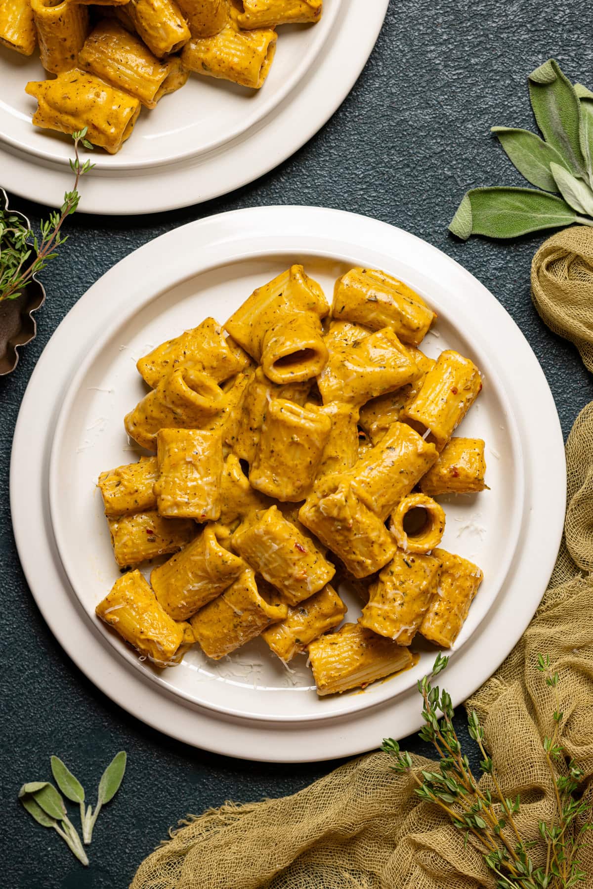 Two plates of creamy pasta on a dark green table with sage leaves. 