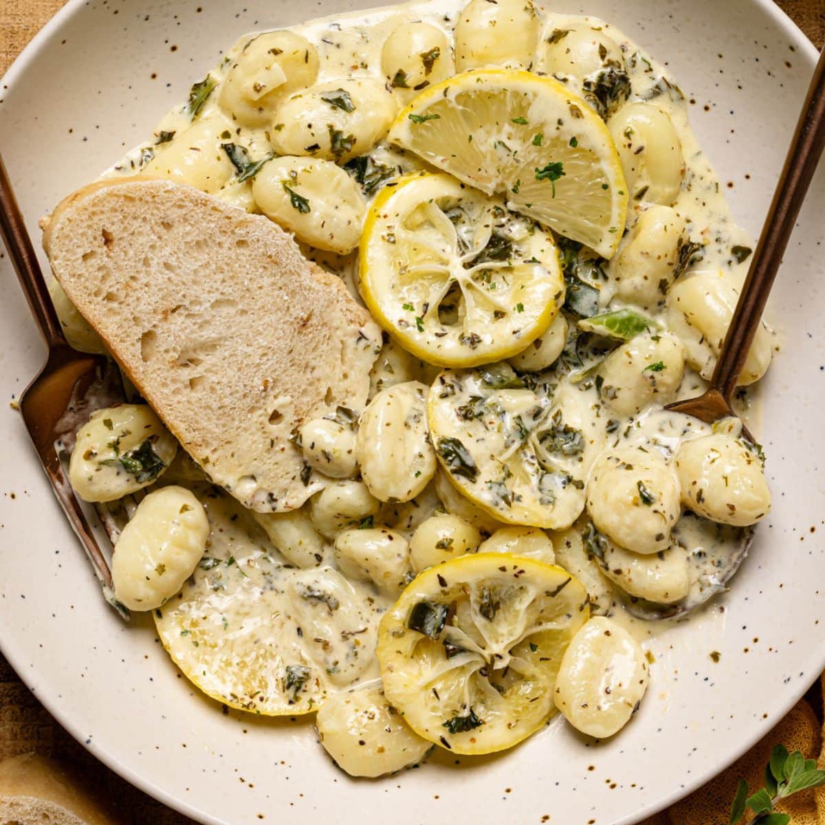 Gnocchi in a plate with a slice of bread, lemon slices, and a spoon + fork.