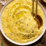 Mashed potatoes in a bowl with two gold spoons and garnish.