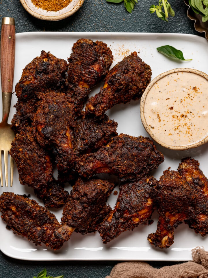 Wings on a white plate with dipping sauce, cajun seasoning, and fork.