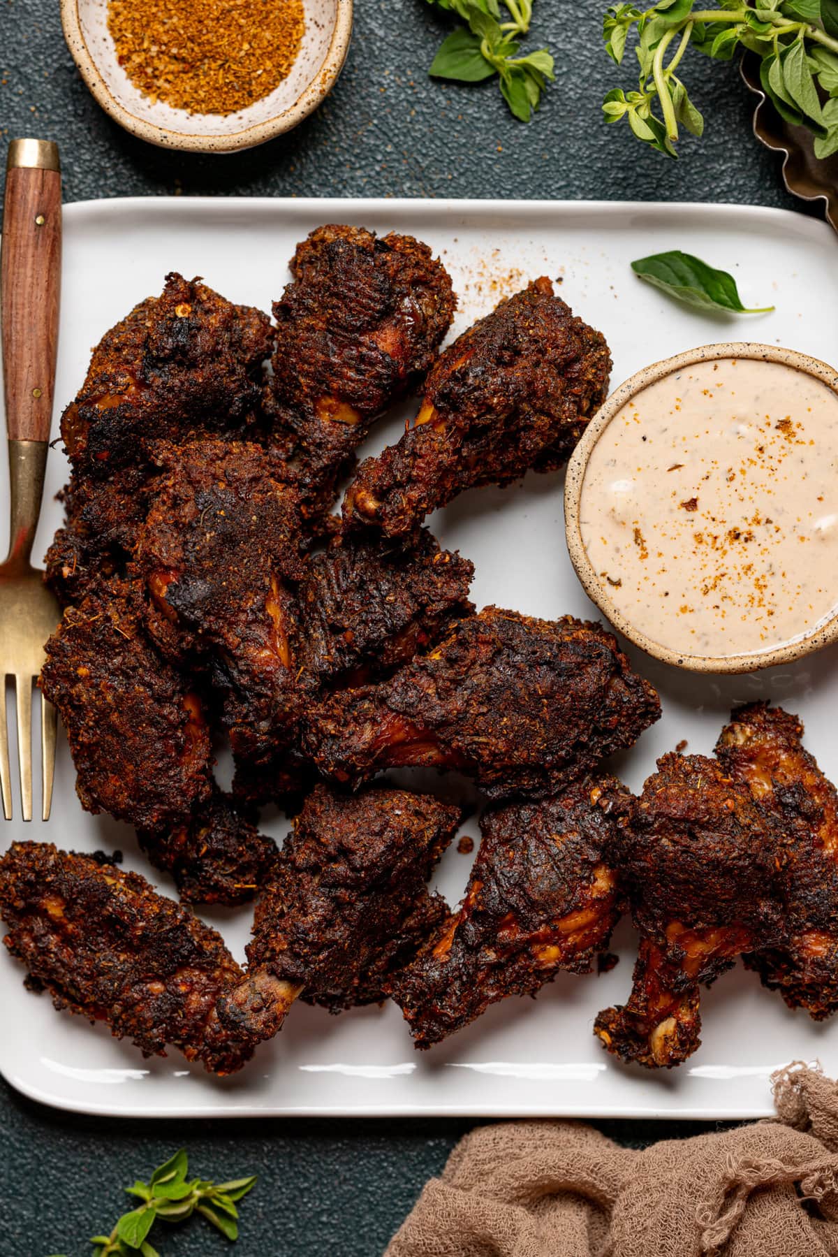 Wings on a white plate with dipping sauce, cajun seasoning, and fork.