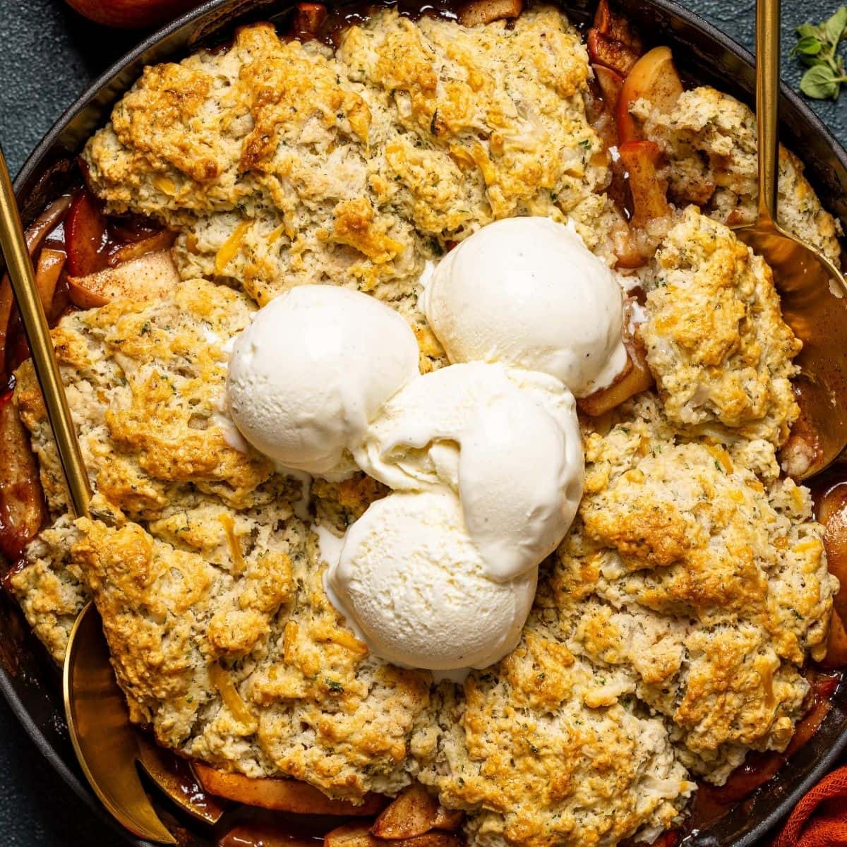 Up close shot of baked cobbler with scoops of ice cream and serving spoons.