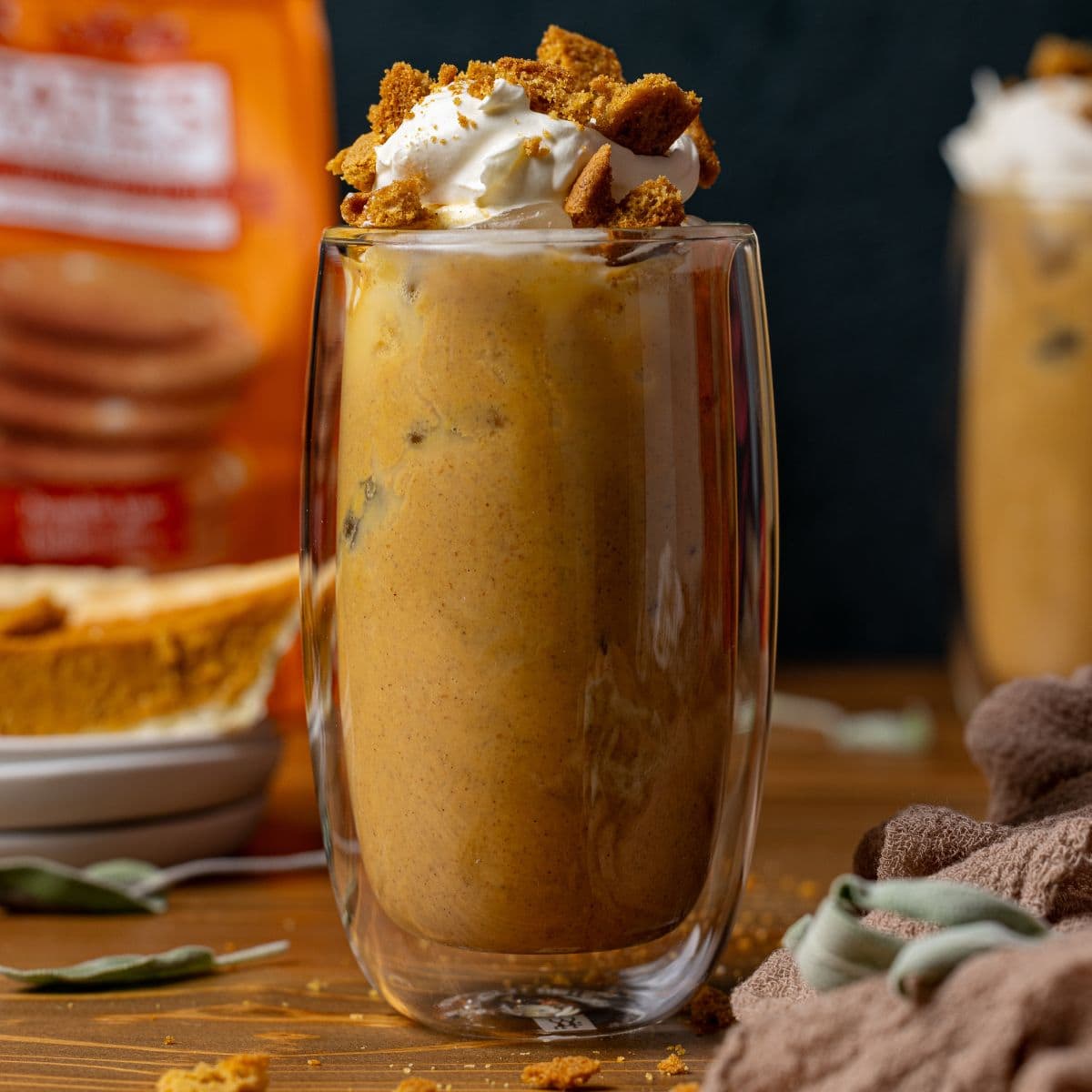 Glass of latte with whipped cream, cookies, a sliced pf pie, and a bag of cookies.