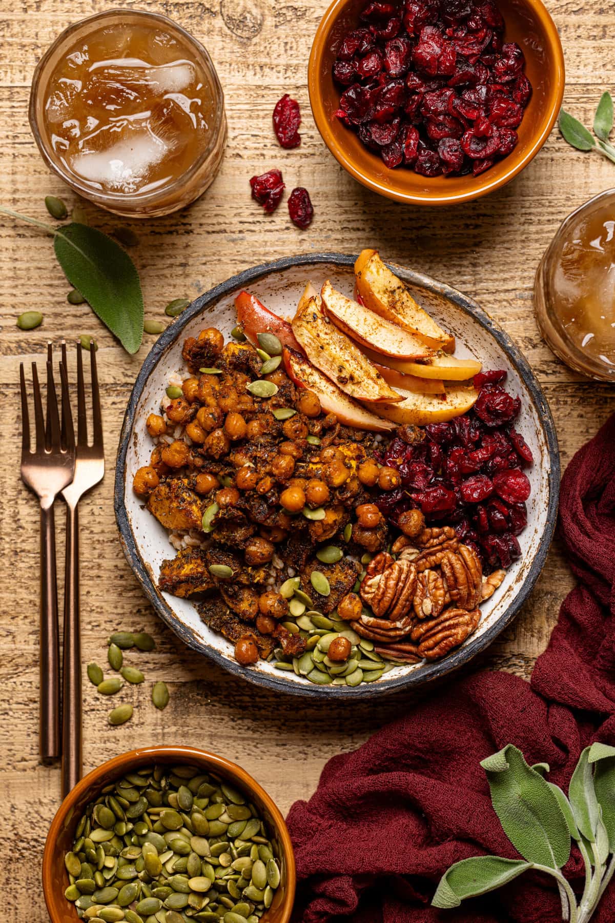 Food bowl with two forks, glass of drink, and bowls on ingredients around it.