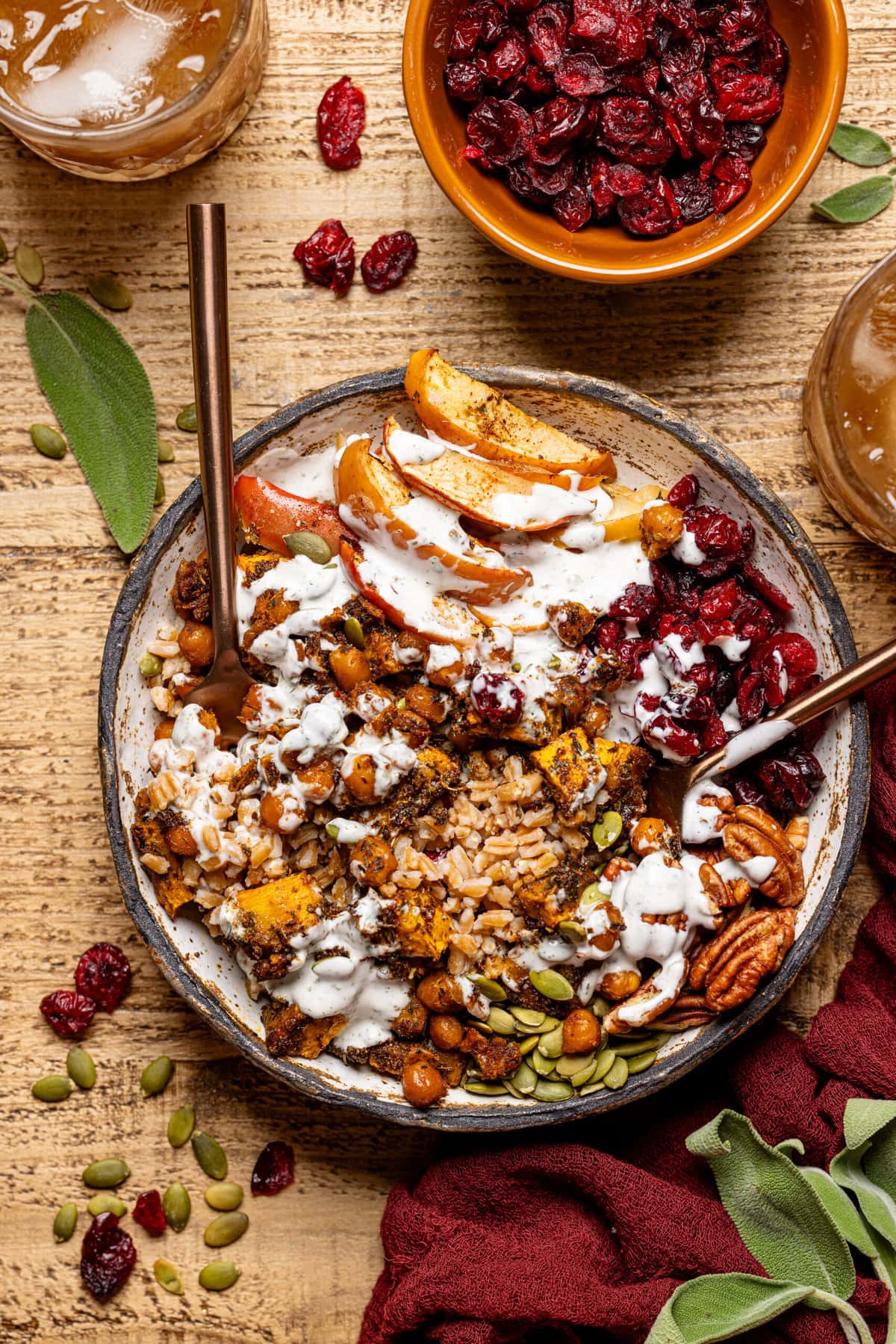 Food bowl on a brown wood table with forks, glass of drink, and bowls of ingredients. 