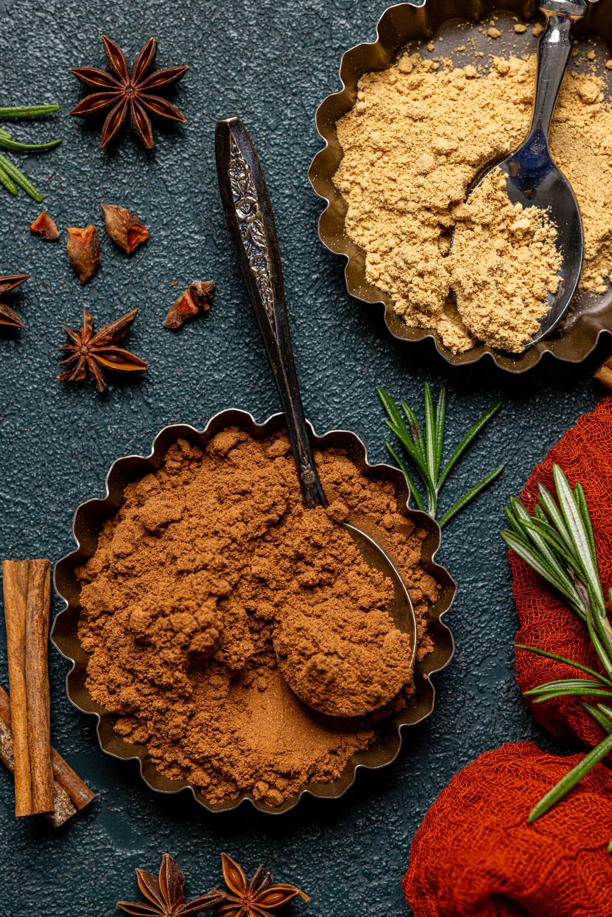 Pumpkin spice and ground ginger in two tins, cinnamon sticks, and rosemary leaves as garnish. 