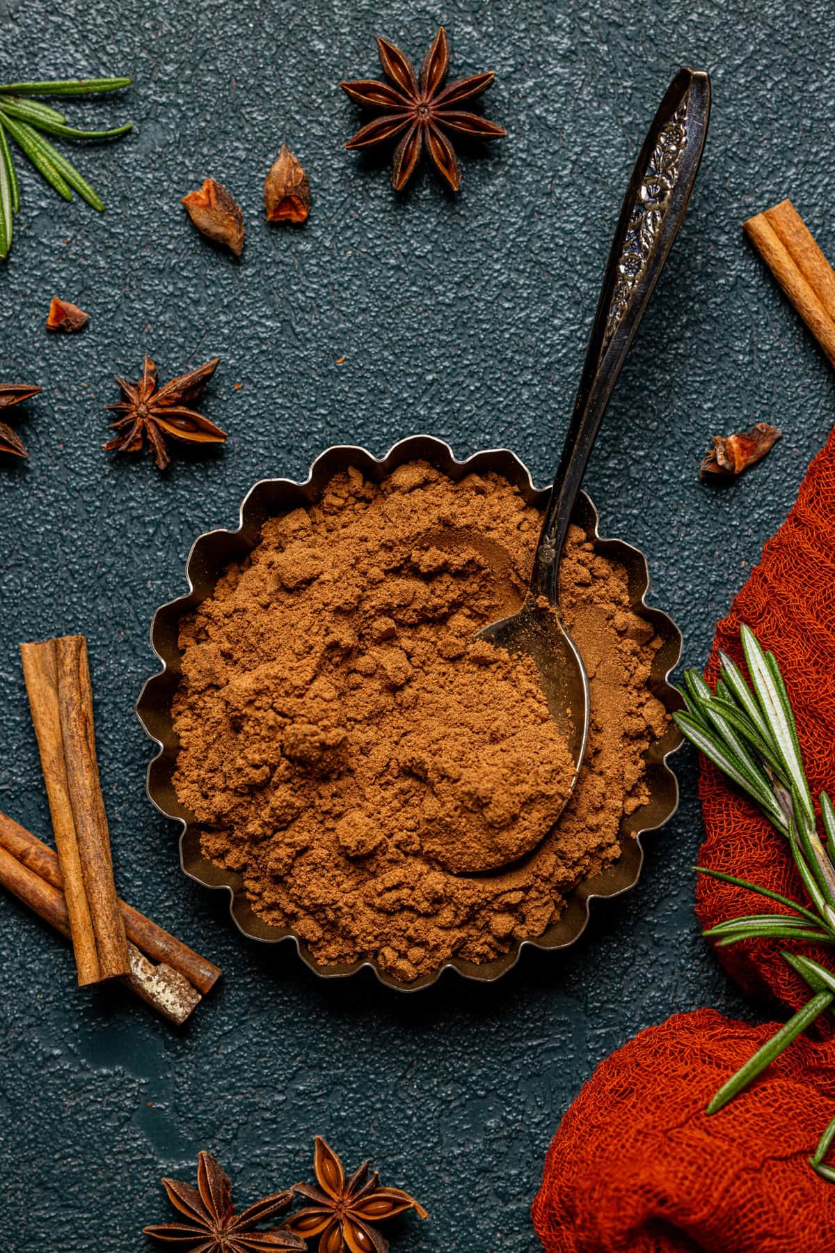 Pumpkin spice in a tin with a spoon on a dark green table.