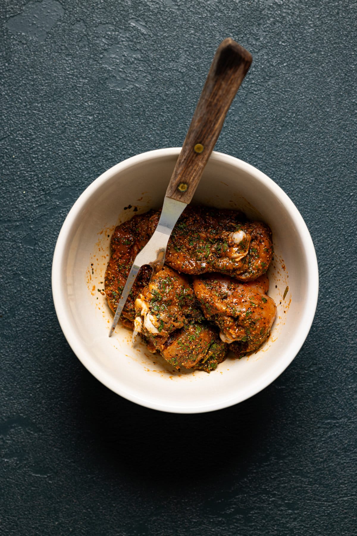 Marinated thighs in a bowl with a fork.