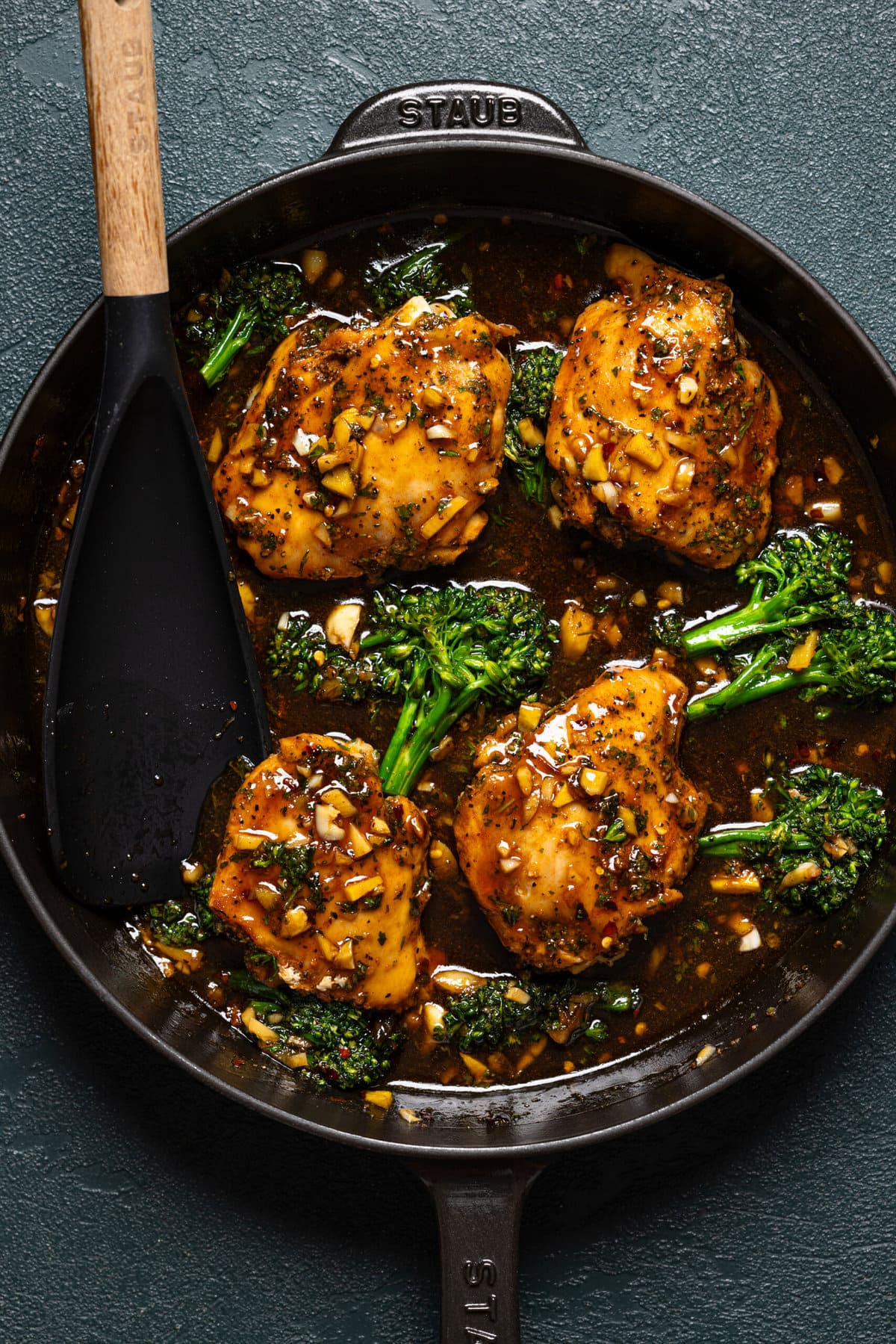 Thighs and broccolini in a black skillet with a black spoon.