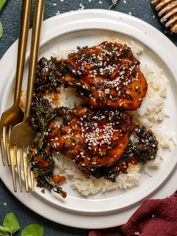 Up close shot of baked chicken and rice in a white plate with two forks.