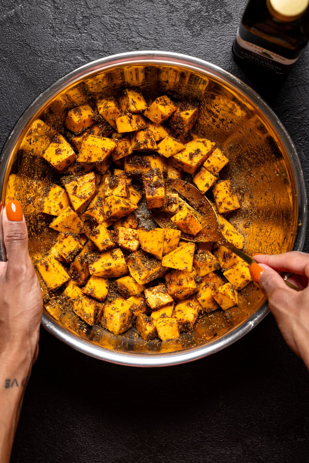 Chopped butternut squash in a bowl being mixed together with olive oil and seasonings. 