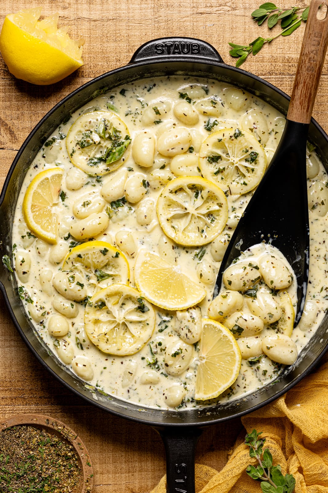 Cooked lemon herb gnocchi in a black skillet with a black spoon.