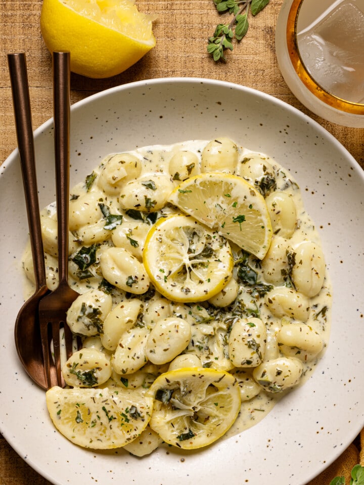 Up close shot of gnocchi in a white plate with fork + spoon.