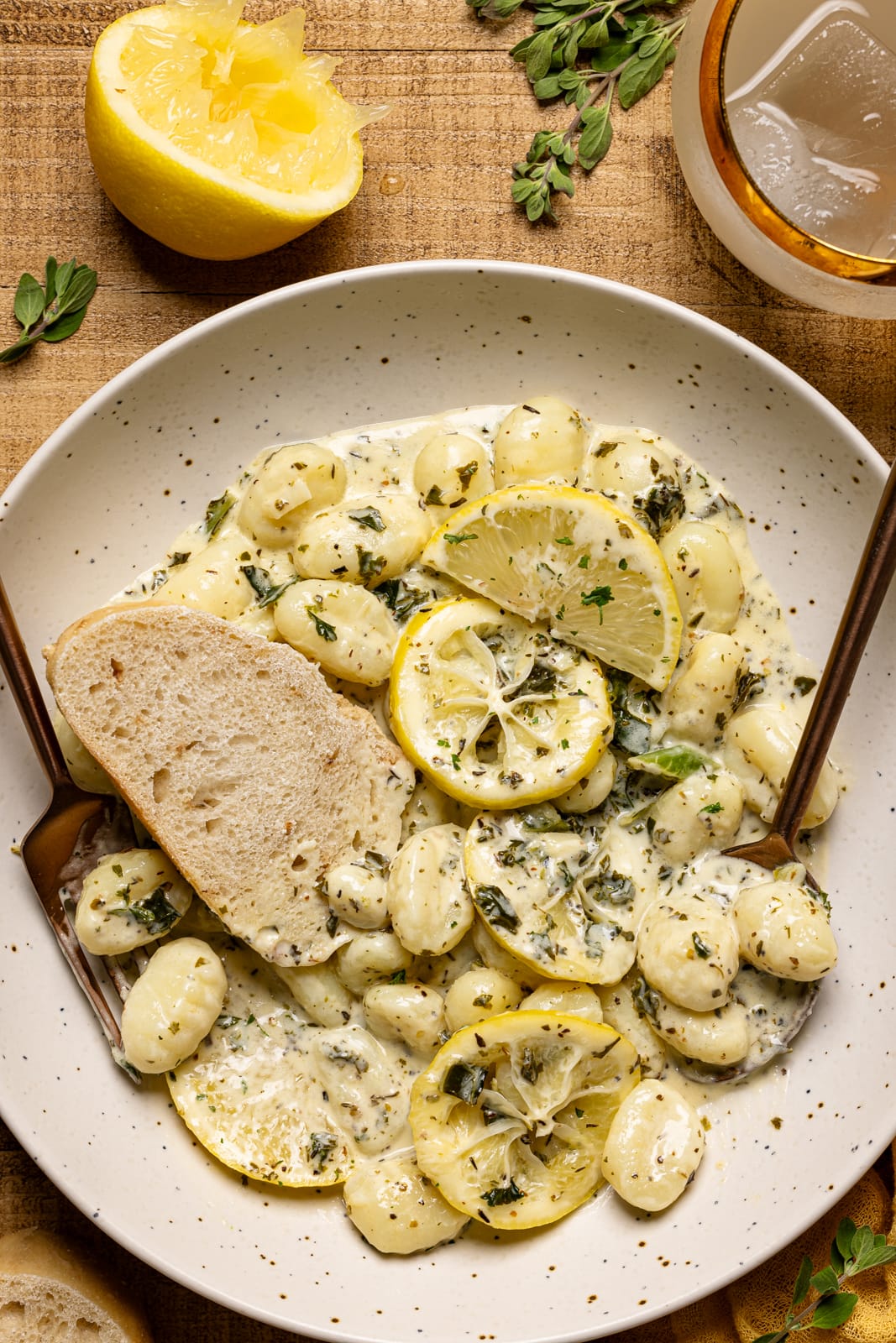 Gnocchi in a plate with a slice of bread, lemon slices, and a spoon + fork.