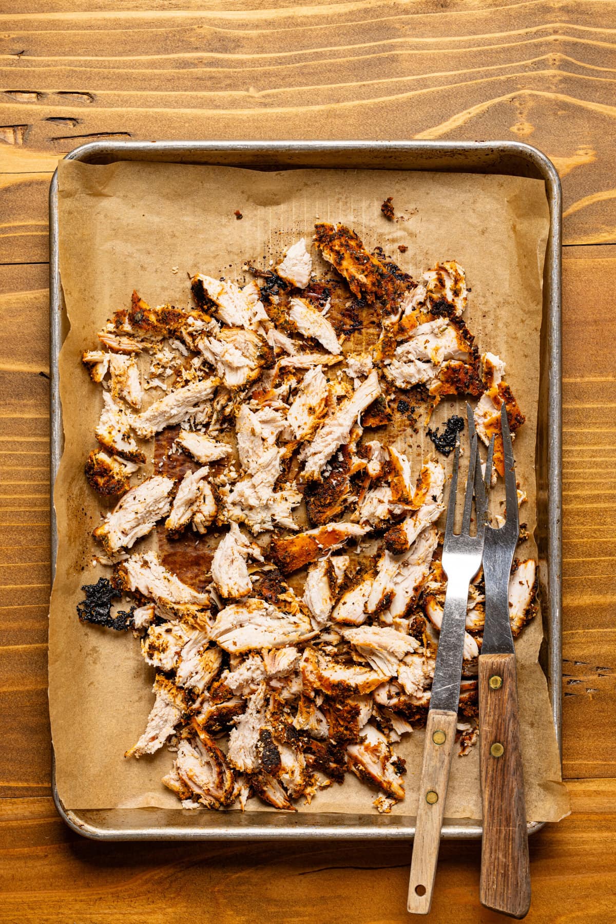 Shredded chicken on a baking sheet with parchment paper and two forks. 