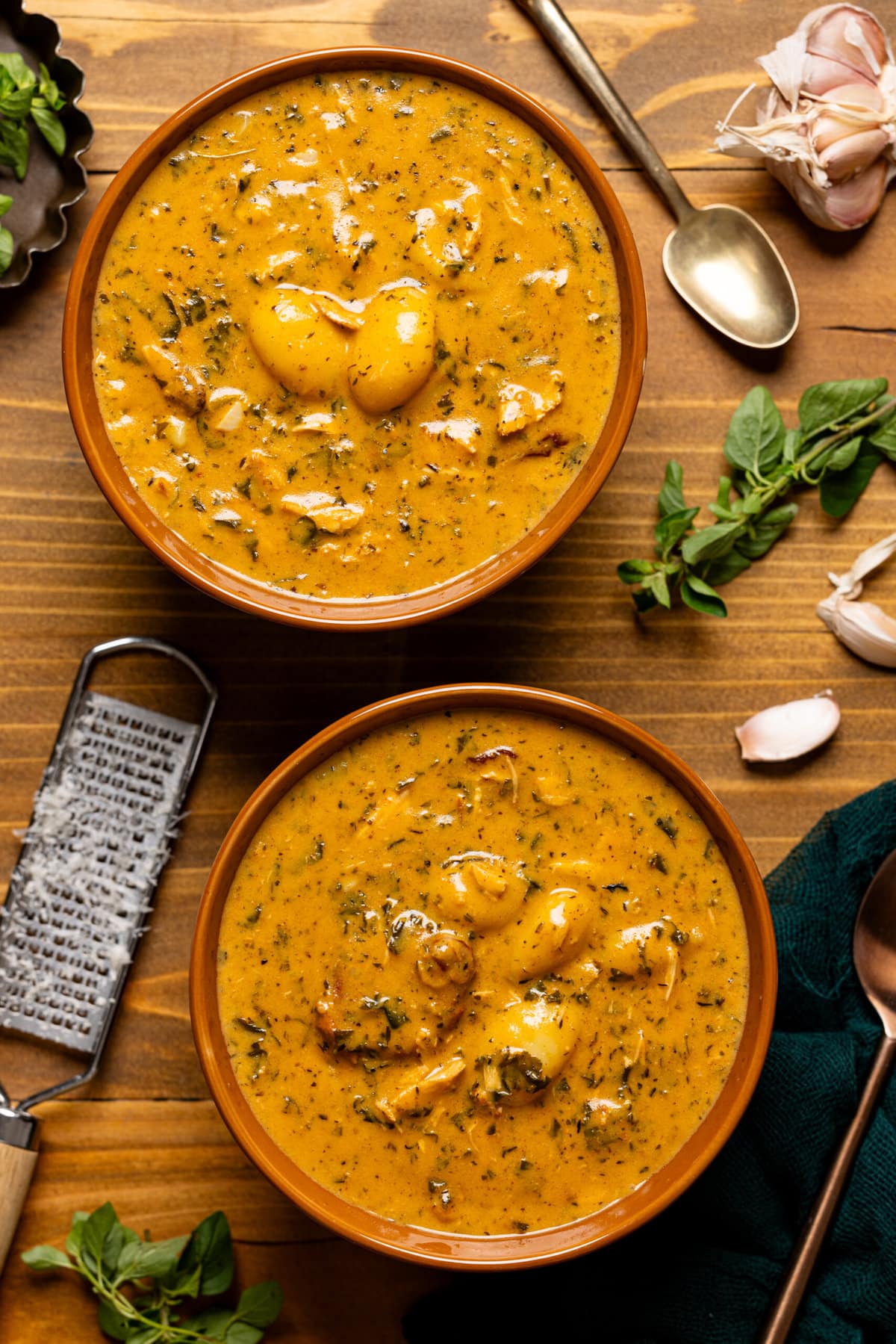 Two bowls of soup on a brown wood table with a grater and garnish.